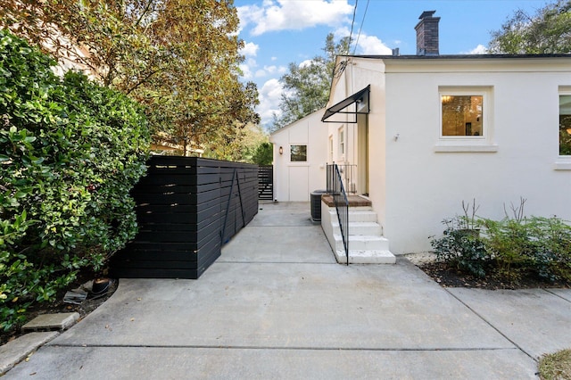 view of side of home with central AC unit, stucco siding, a chimney, and fence