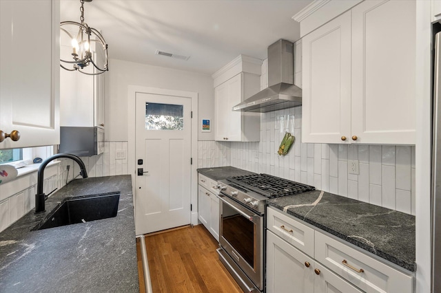 kitchen with wood finished floors, a sink, high end stainless steel range, wall chimney range hood, and tasteful backsplash