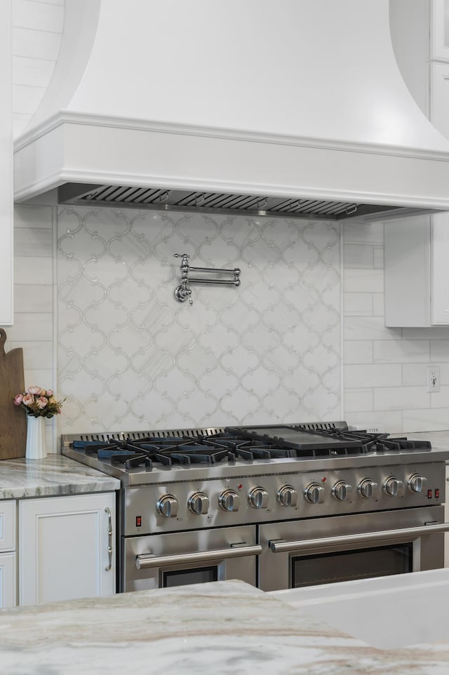 1130 Plantation Overlook Dr, Moncks Corner, SC 29461 - kitchen with range with two ovens, custom exhaust hood, tasteful backsplash, white cabinets, and light stone counters