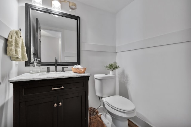 half bathroom with baseboards, vanity, and toilet