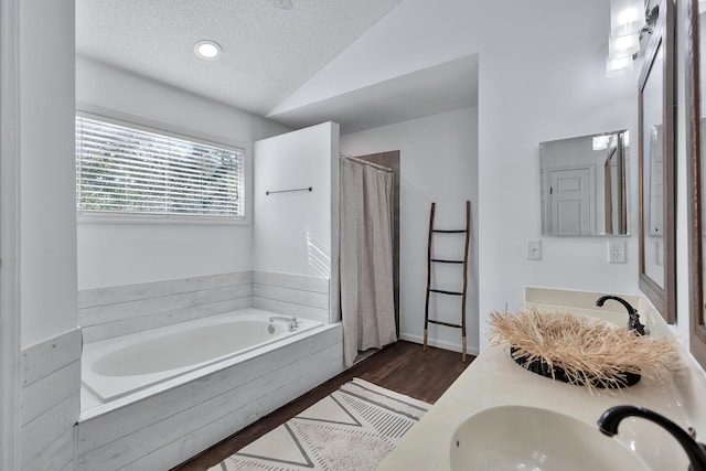 full bath with lofted ceiling, a textured ceiling, wood finished floors, a sink, and a bath