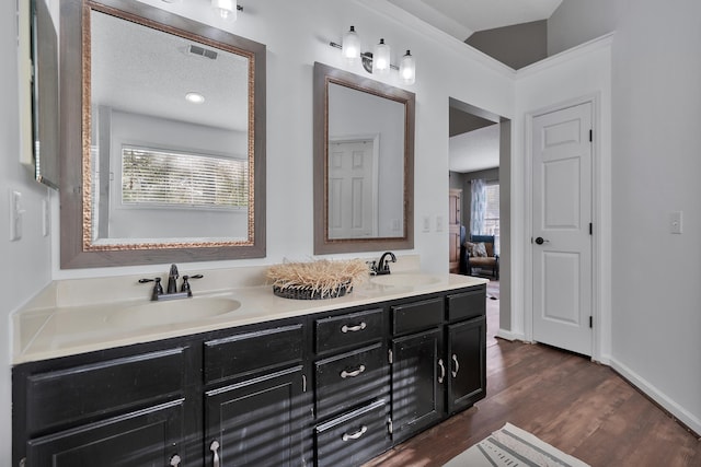 full bath with double vanity, wood finished floors, a sink, and baseboards