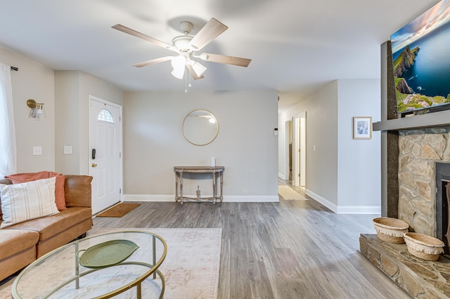 unfurnished living room featuring a fireplace, a ceiling fan, baseboards, and wood finished floors