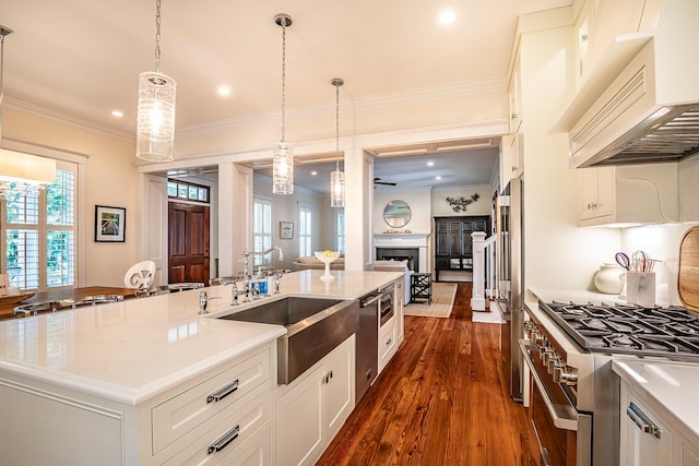 kitchen featuring premium range hood, decorative light fixtures, a kitchen island with sink, white cabinetry, and sink