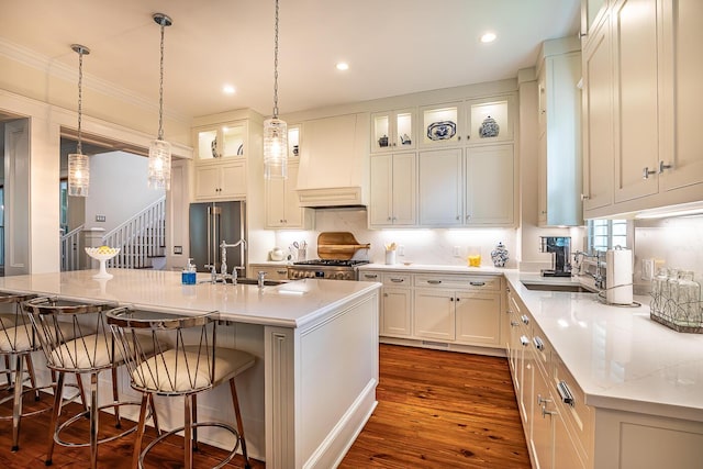 kitchen featuring custom exhaust hood, light stone countertops, a center island with sink, high end refrigerator, and dark wood-type flooring