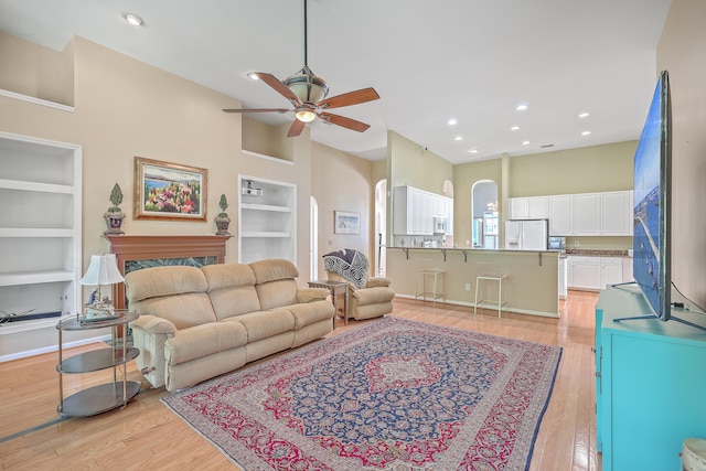 living room featuring built in shelves, light hardwood / wood-style flooring, and ceiling fan