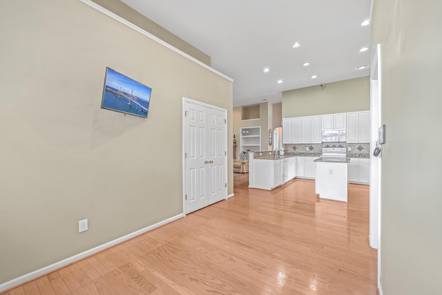 kitchen with kitchen peninsula, tasteful backsplash, white appliances, white cabinets, and light hardwood / wood-style floors