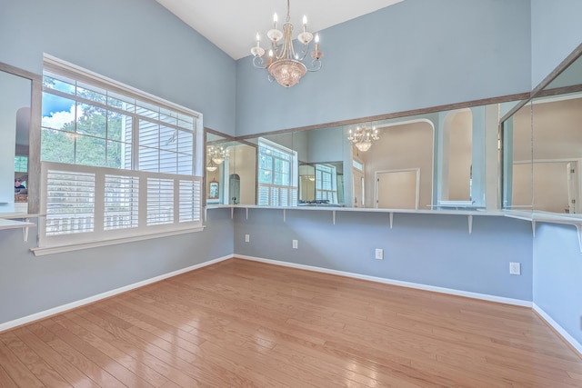 spare room with light hardwood / wood-style flooring, a high ceiling, and an inviting chandelier