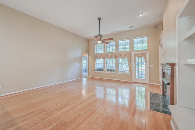 unfurnished living room with ceiling fan, a premium fireplace, a towering ceiling, and light hardwood / wood-style flooring