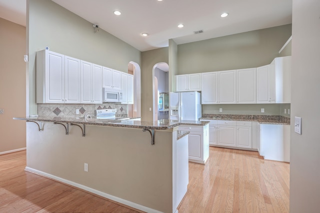 kitchen featuring white cabinetry, dark stone counters, white appliances, light hardwood / wood-style floors, and a breakfast bar