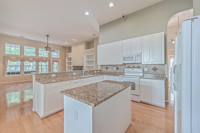 kitchen with decorative light fixtures, a kitchen island, white appliances, and kitchen peninsula