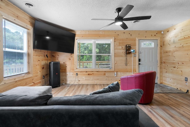 living room featuring a textured ceiling, hardwood / wood-style floors, wooden walls, and ceiling fan