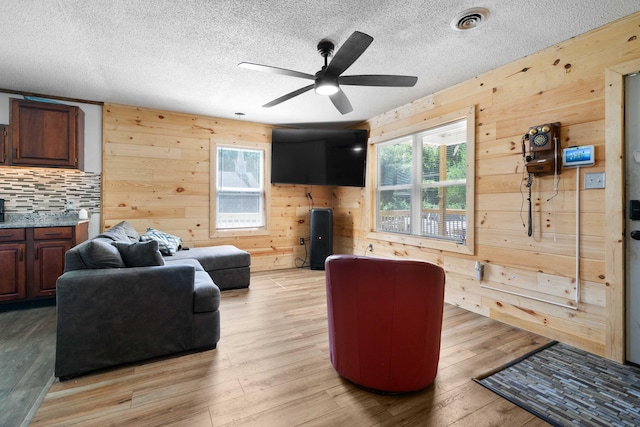 living room featuring light hardwood / wood-style flooring, wood walls, a textured ceiling, and ceiling fan