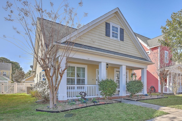 bungalow-style home with roof with shingles, covered porch, a front yard, and fence