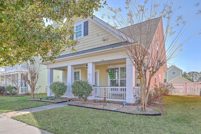 view of front of house featuring a porch, roof with shingles, a front lawn, and fence