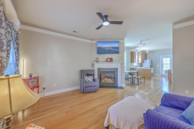 living area with visible vents, a fireplace with flush hearth, ornamental molding, light wood-style floors, and baseboards