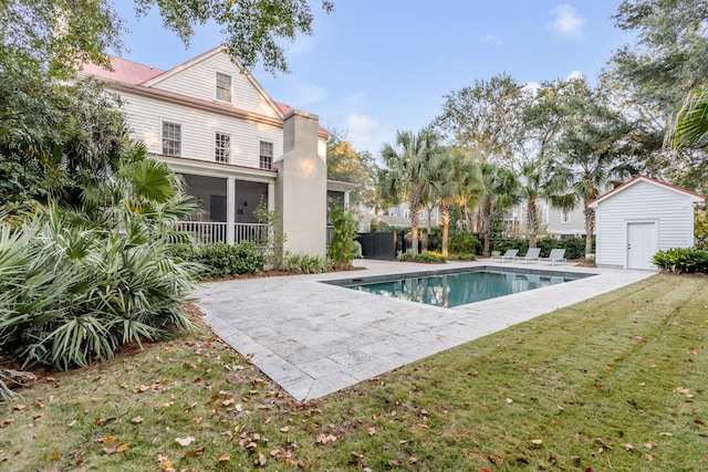 view of swimming pool featuring a patio, a storage unit, a lawn, and a sunroom