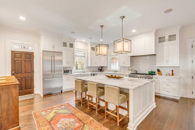 kitchen featuring stainless steel appliances, wood-type flooring, white cabinets, a kitchen island, and hanging light fixtures