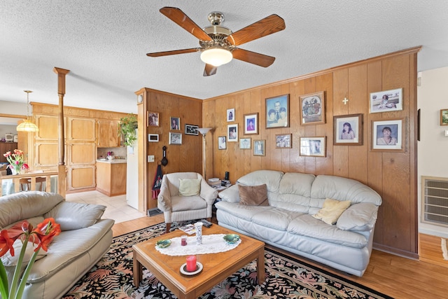 living area with wooden walls, ceiling fan, a textured ceiling, and light wood finished floors