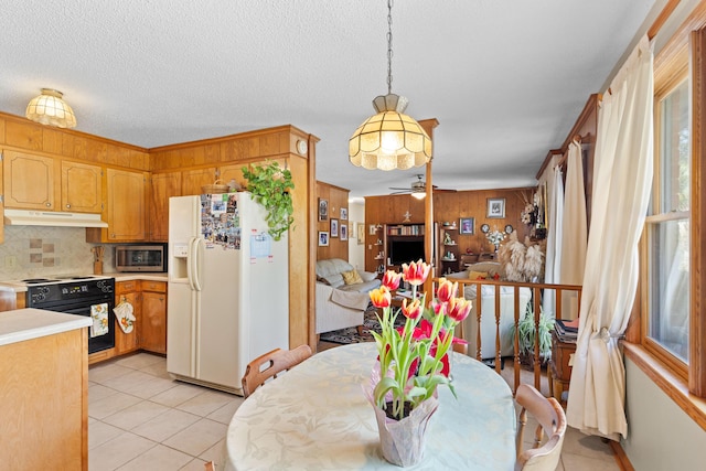 dining space with light tile patterned floors, a textured ceiling, a ceiling fan, and wooden walls