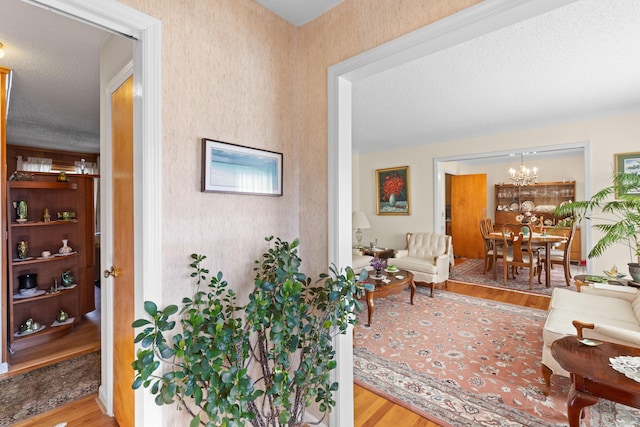 hallway with a textured ceiling, wood finished floors, and an inviting chandelier