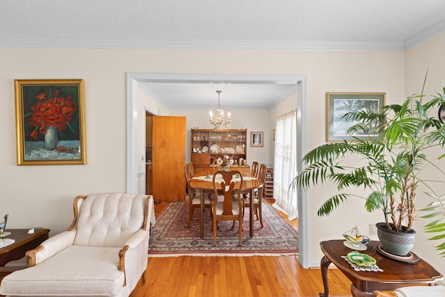 dining area featuring light wood-style floors, ornamental molding, a chandelier, and a textured ceiling