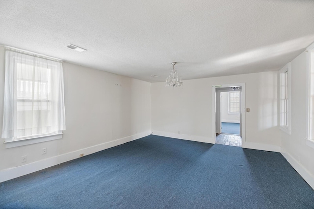 spare room with a wealth of natural light, visible vents, dark carpet, and a textured ceiling