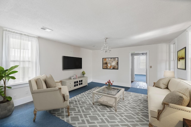 living area featuring a chandelier, visible vents, a textured ceiling, and baseboards