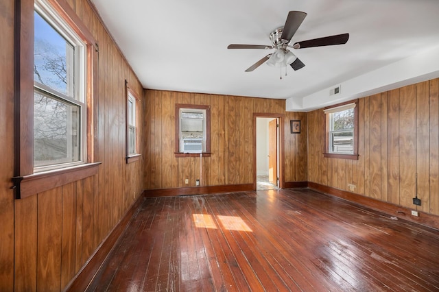 empty room featuring dark wood-style floors, visible vents, wooden walls, cooling unit, and baseboards