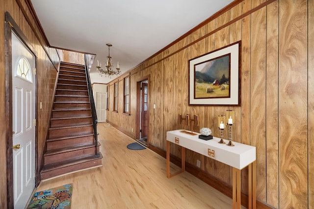 foyer with light wood finished floors, wooden walls, stairway, crown molding, and a notable chandelier