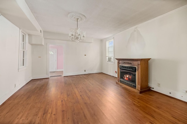 unfurnished living room with an inviting chandelier, baseboards, wood finished floors, and a glass covered fireplace