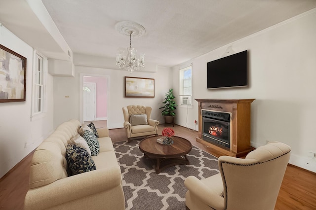 living room featuring a glass covered fireplace, an inviting chandelier, and wood finished floors