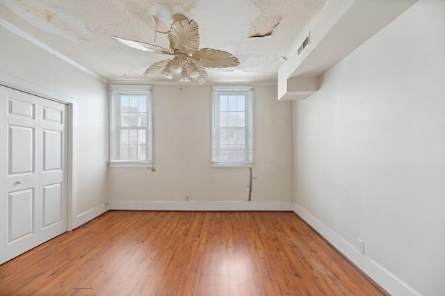 unfurnished bedroom featuring light wood-style floors, ornamental molding, a textured ceiling, and baseboards