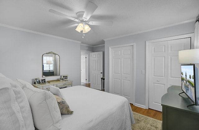 bedroom featuring crown molding, multiple closets, ceiling fan, wood finished floors, and baseboards