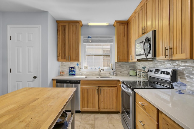 kitchen featuring decorative backsplash, appliances with stainless steel finishes, brown cabinets, wooden counters, and a sink