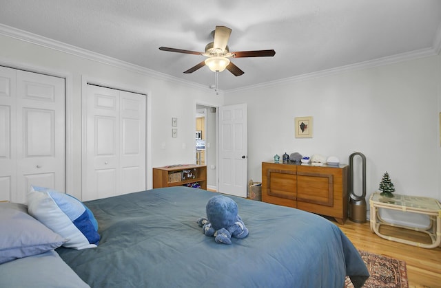 bedroom with wood finished floors, two closets, and crown molding