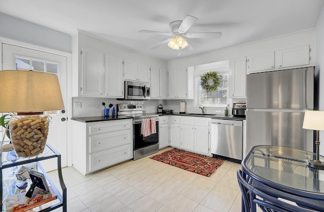 kitchen with white cabinets, dark countertops, a sink, stainless steel appliances, and backsplash