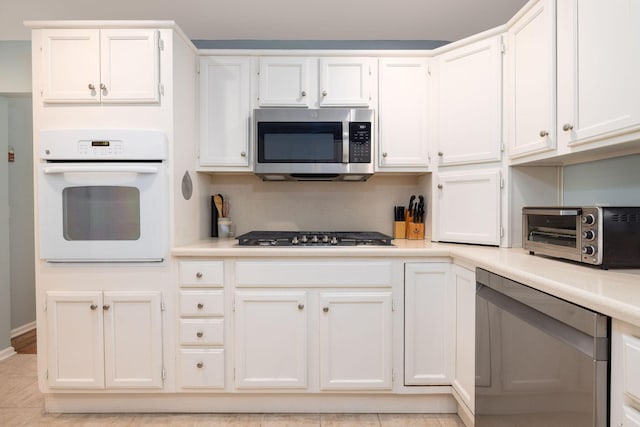 kitchen with light tile patterned floors, a toaster, white cabinetry, light countertops, and appliances with stainless steel finishes