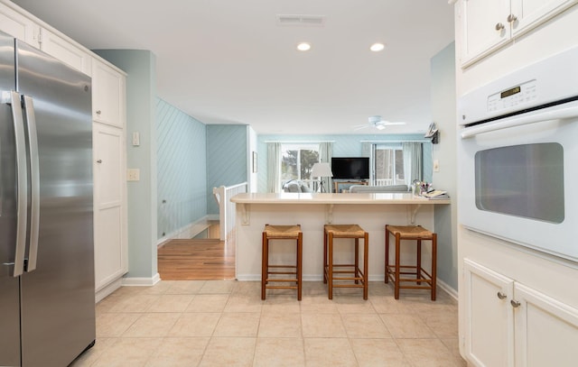 kitchen featuring a breakfast bar, freestanding refrigerator, oven, and light tile patterned flooring