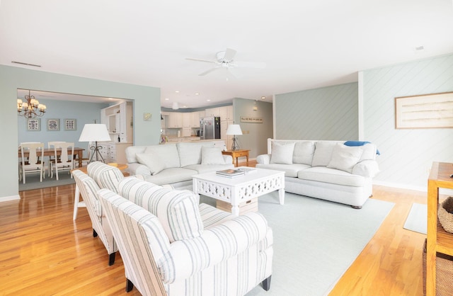 living area featuring light wood-style flooring, visible vents, baseboards, and ceiling fan with notable chandelier