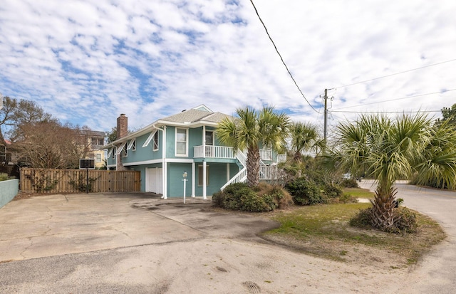 beach home featuring a porch, concrete driveway, fence, and stairway