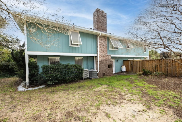 back of house with central AC unit, a lawn, a chimney, fence, and brick siding