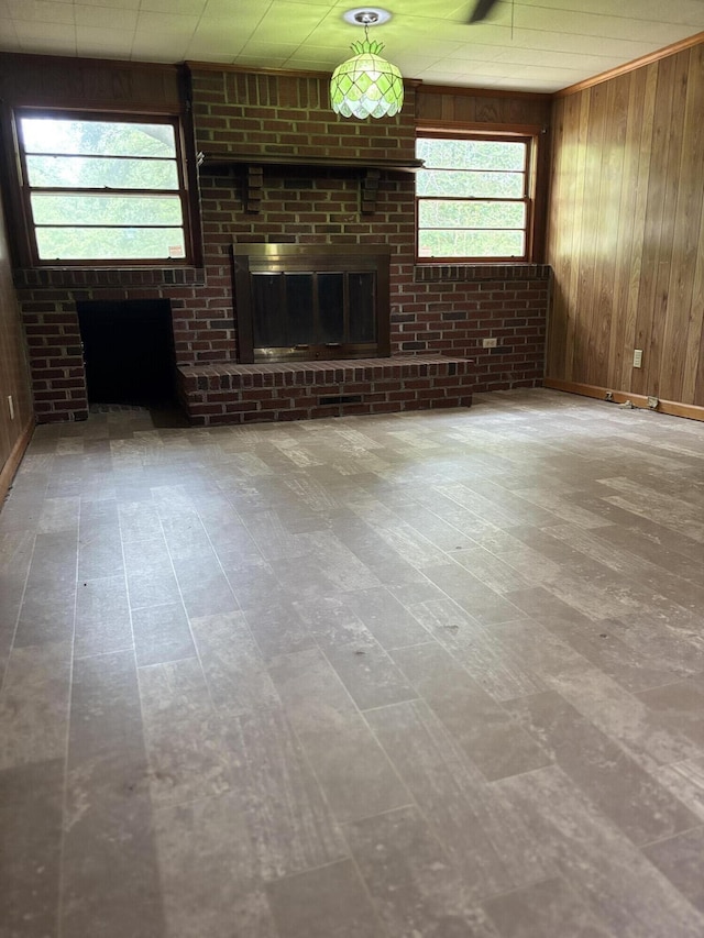 unfurnished living room with a brick fireplace, wooden walls, baseboards, and wood finished floors