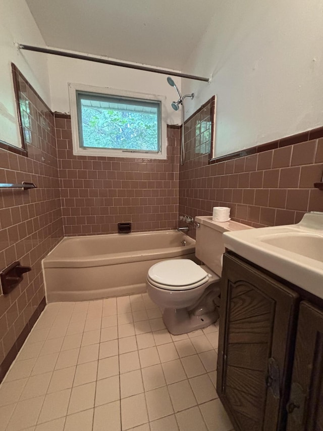 bathroom with tile walls, tile patterned flooring, tub / shower combination, toilet, and wainscoting