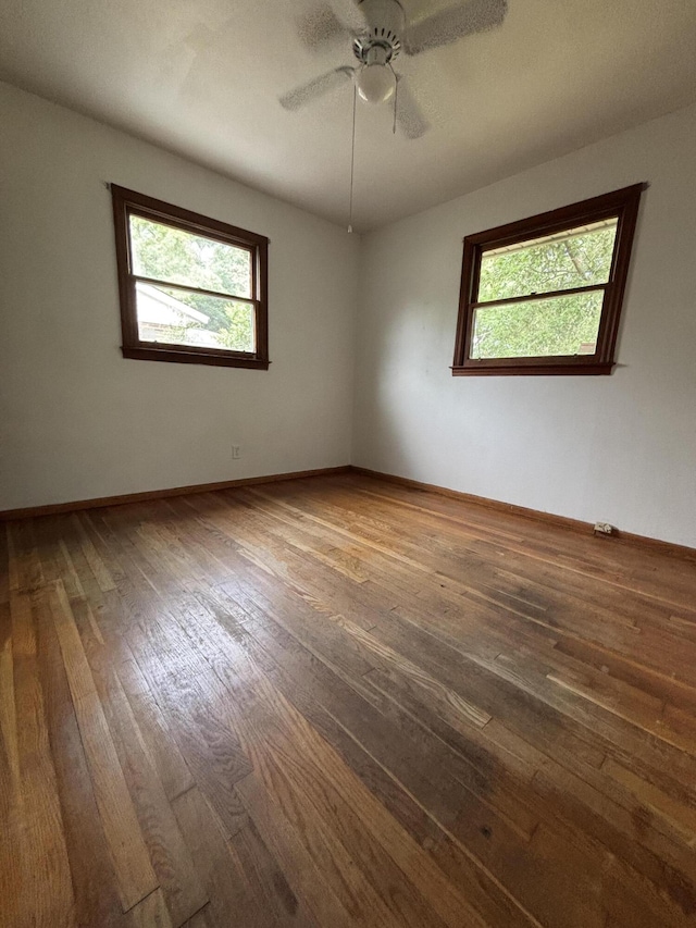 empty room with plenty of natural light, dark wood-style flooring, a ceiling fan, and baseboards