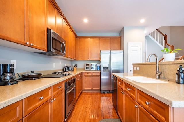 kitchen featuring light stone counters, sink, black appliances, and light hardwood / wood-style flooring