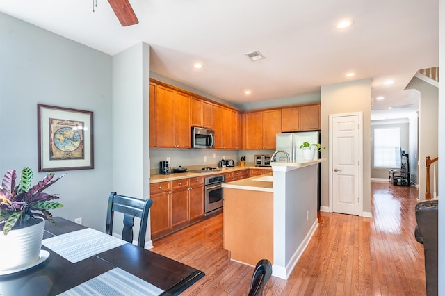 kitchen with light wood-type flooring, stainless steel appliances, ceiling fan, a kitchen island with sink, and sink