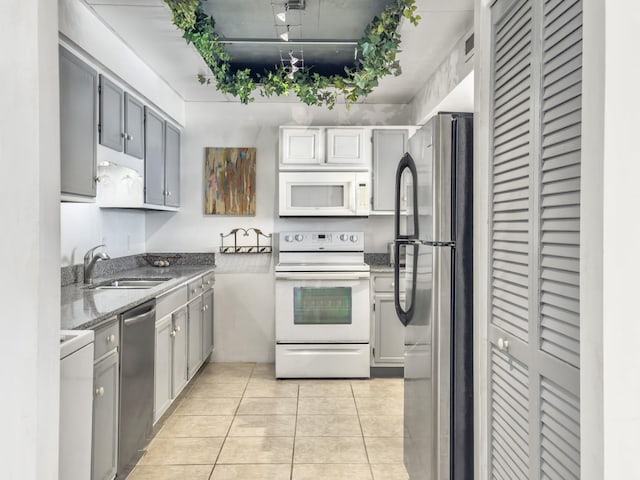 kitchen with light tile patterned floors, dark stone counters, a sink, stainless steel appliances, and track lighting