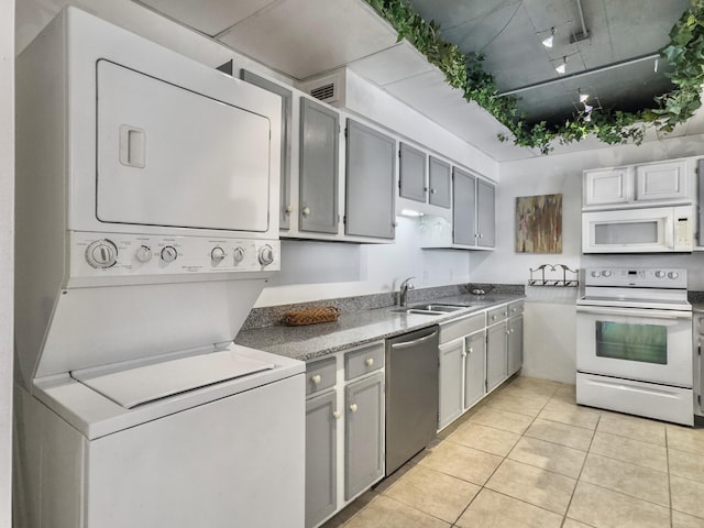 kitchen with white appliances, light tile patterned floors, stacked washer / drying machine, gray cabinets, and a sink