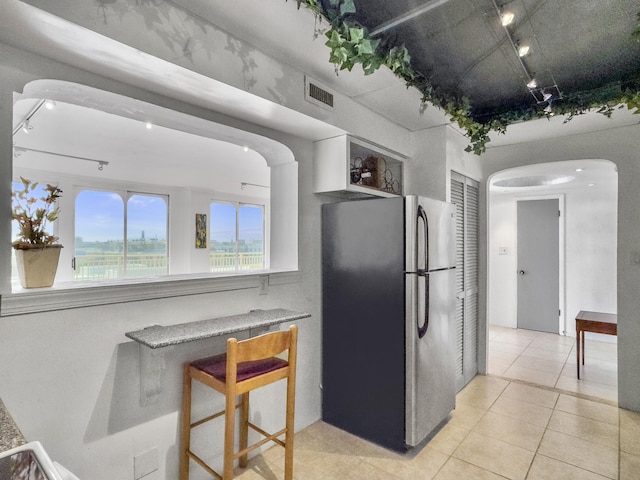 kitchen featuring arched walkways, visible vents, freestanding refrigerator, light tile patterned flooring, and track lighting